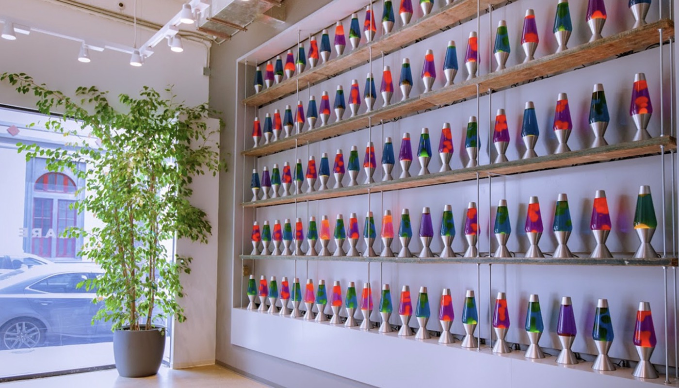 A wall of dozens of colorful lava lamps arranged on shelves in an office lobby